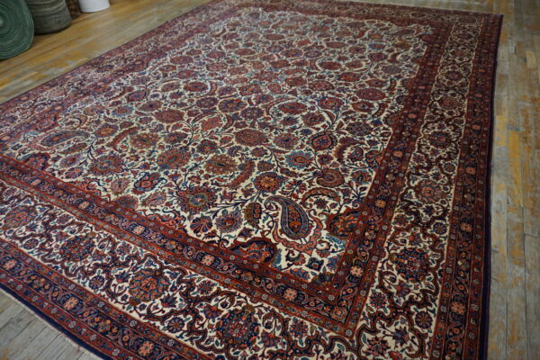Large traditional ivory rug with dense red and blue floral patterns covers a worn wood plank floor.