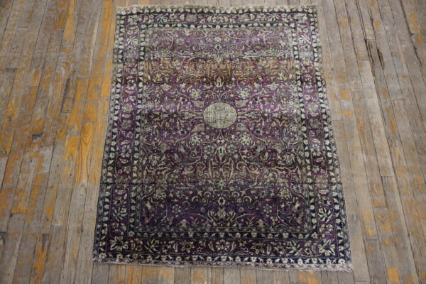 Intricate purple rug with cream and gold floral motifs, featuring a central medallion on distressed wood floors.