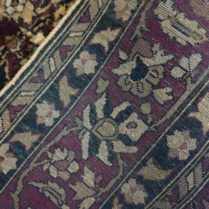 Rolled rug displays its plush pile and tight woven backing with burgundy, blue, and tan floral patterns.