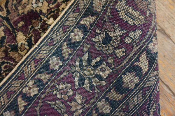 Rolled rug displays its plush pile and tight woven backing with burgundy, blue, and tan floral patterns.