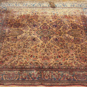 Low pile rug with a dense gold and red floral pattern and wide blue-green border on wood flooring.