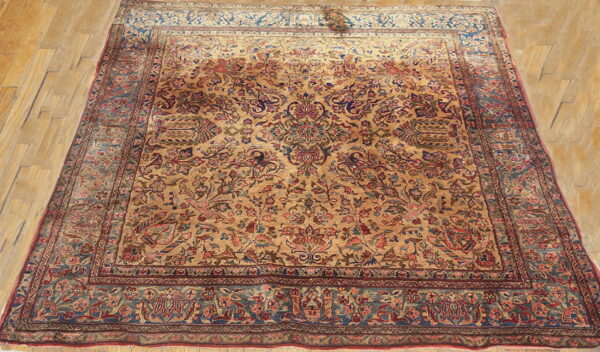 Low pile rug with a dense gold and red floral pattern and wide blue-green border on wood flooring.