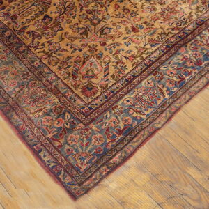Ornate gold rug corner showing a blue and red floral border on light plank wood flooring.
