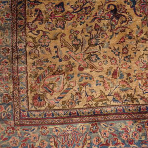 Detailed view of a gold rug field patterned with red and pink florals and a wide blue border.