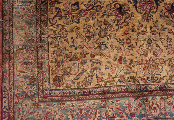Detailed view of a gold rug field patterned with red and pink florals and a wide blue border.