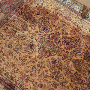 Ornate area rug with a golden field and detailed botanical motifs in faded red and deep blue.