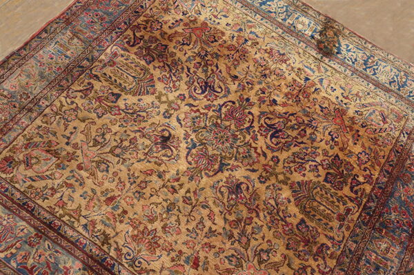 Ornate area rug with a golden field and detailed botanical motifs in faded red and deep blue.