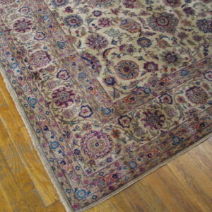 Detailed view of a traditional beige rug with magenta and blue floral patterns on wood plank flooring.