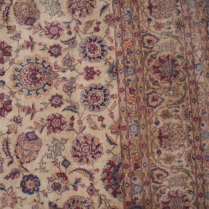 Traditional beige rug featuring low pile floral and medallion patterns accented in maroon, blue, and gold.