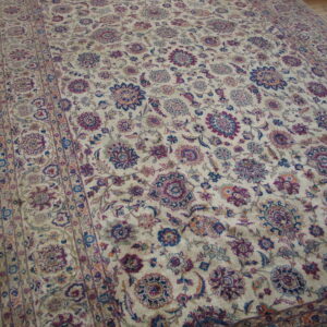 Large low-pile rug with a detailed floral pattern in ivory, maroon, and dark blue on wood planks.