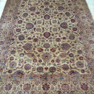 Traditional rug with a dense beige field, patterned with maroon and navy florals, laying on light tiles.