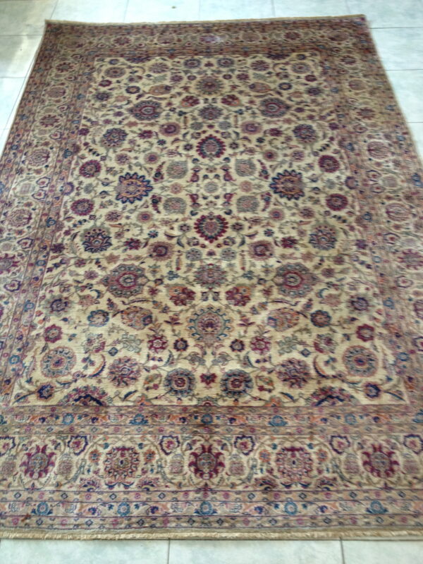 Traditional rug with a dense beige field, patterned with maroon and navy florals, laying on light tiles.
