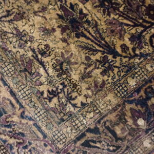 Low-pile rug corner featuring gold field, navy, and purple floral motifs with tassels on wood flooring.