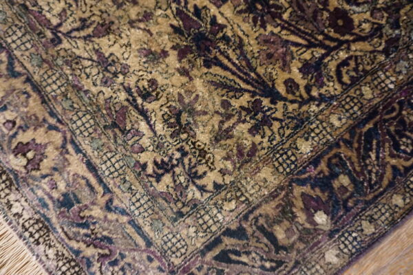 Low-pile rug corner featuring gold field, navy, and purple floral motifs with tassels on wood flooring.