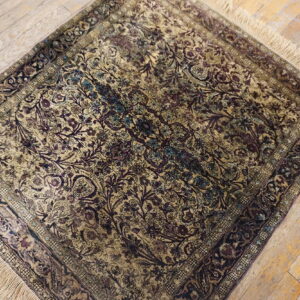 A small low-pile rug featuring dense plum, gold, and teal floral patterns sits on distressed wood floors.