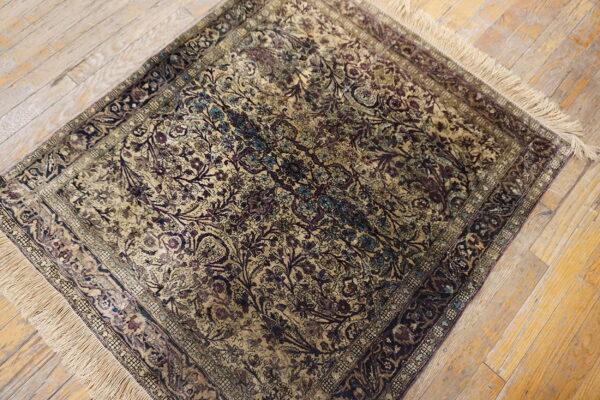 A small low-pile rug featuring dense plum, gold, and teal floral patterns sits on distressed wood floors.