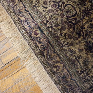 Ornate gold and purple patterned rug with fringe rests on distressed light wood floorboards.