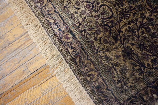 Ornate gold and purple patterned rug with fringe rests on distressed light wood floorboards.