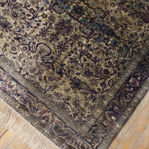 Muted beige rug with complex purple and blue traditional patterns rests on rustic wood plank flooring.