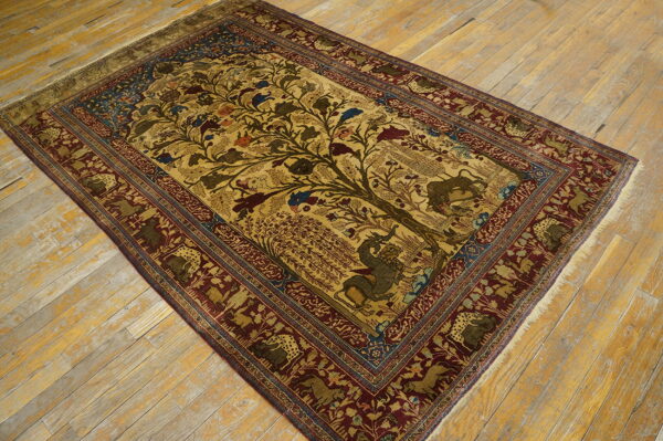 Gold tree of life rug with animal motifs and a deep red border rests on distressed light wood flooring.