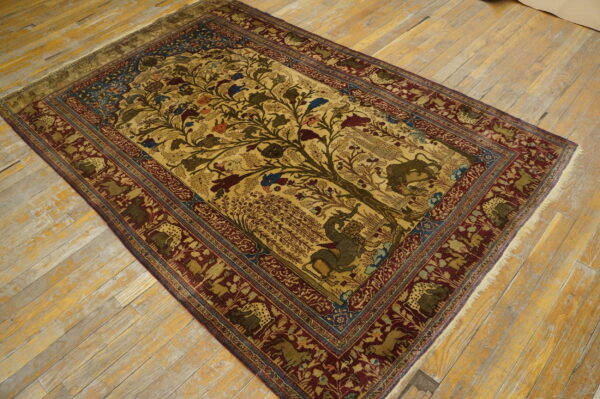 Gold and burgundy rug with a detailed tree of life and animal pattern rests on worn wood planks.