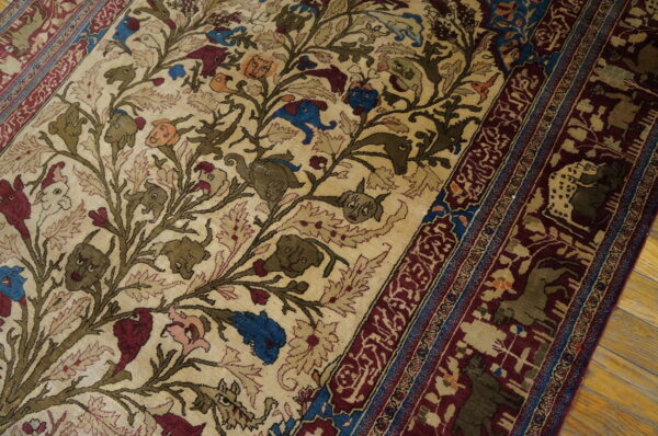 Close-up of a beige rug with stylized animal heads, vines, and a deep burgundy patterned border on wood flooring.