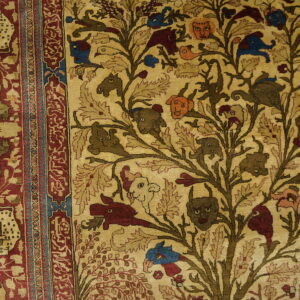 Beige rug featuring a detailed Tree of Life with animals and faces, bordered in red, placed on wood planks.