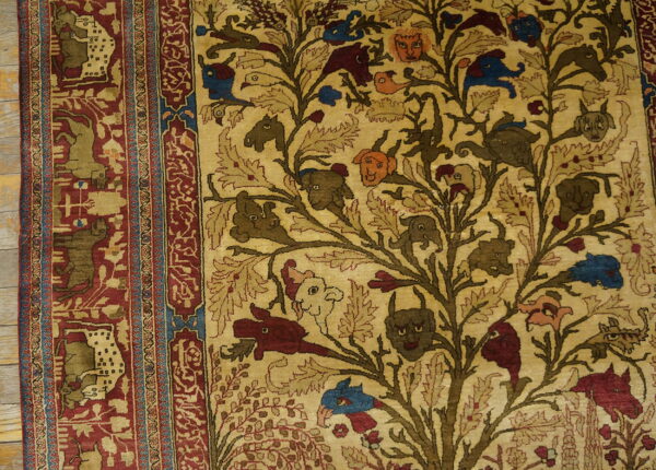 Beige rug featuring a detailed tree of life with animals and faces, bordered in red, placed on wood planks.
