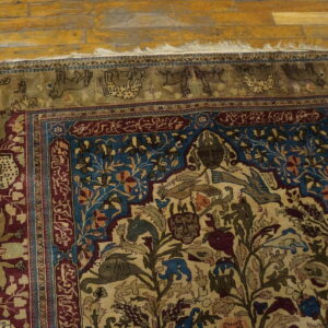 Complex tan, blue, and burgundy rug featuring human and animal motifs, placed on golden wood floors.