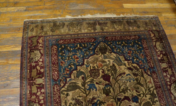Complex tan, blue, and burgundy rug featuring human and animal motifs, placed on golden wood floors.