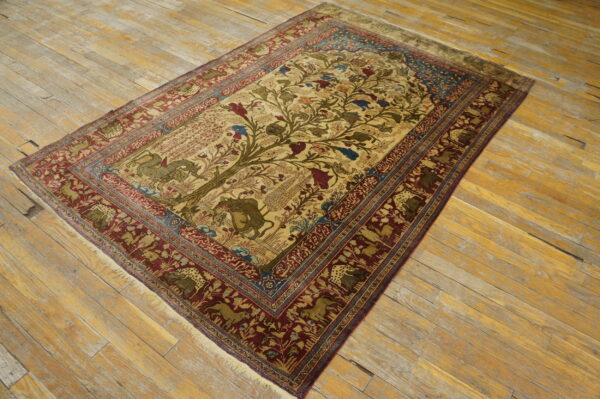 Beige rug featuring a detailed tree of life design and deep maroon border on worn wood flooring.