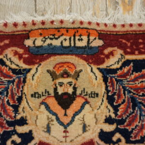 Close-up of a red and navy rug featuring a bearded figure motif under calligraphy, with fringe on light wood.