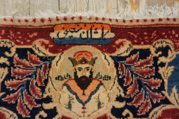 Close-up of a red and navy rug featuring a bearded figure motif under calligraphy, with fringe on light wood.