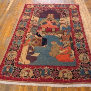 Red and blue figural rug with a central court scene and portrait border on light hardwood floors.