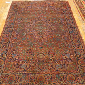 A large red and navy rug with a dense traditional floral pattern rests on light hardwood floors.