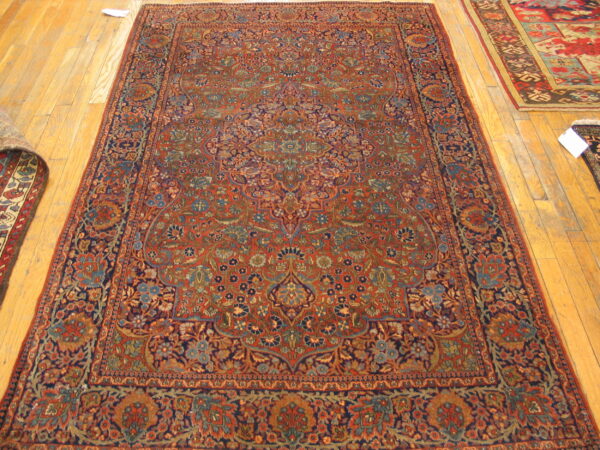 A large red and navy rug with a dense traditional floral pattern rests on light hardwood floors.
