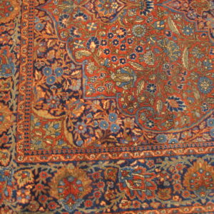 Red-orange rug field and navy blue floral border featuring secondary colors of light blue and tan.