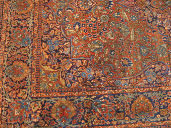 Red-orange rug field and navy blue floral border featuring secondary colors of light blue and tan.