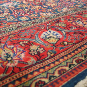 Low pile rug featuring traditional blue field and red border with cream, yellow, and red floral motifs.