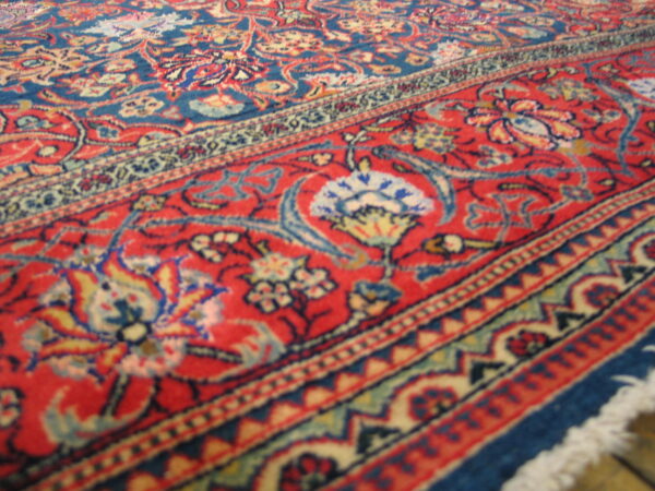 Low pile rug featuring traditional blue field and red border with cream, yellow, and red floral motifs.