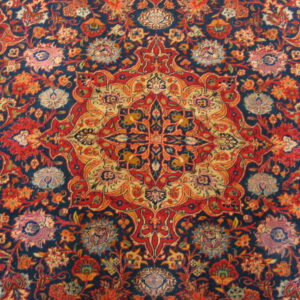 Intricate traditional rug pattern featuring a dense floral medallion motif in navy, red, and gold.