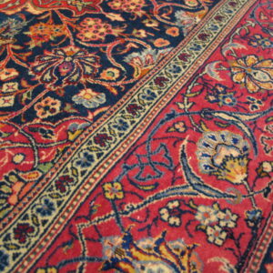 Angled close-up of a detailed rug pattern featuring red and navy blue fields separated by a cream floral border.