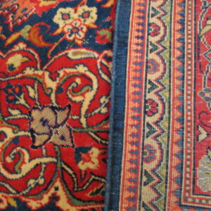 Detailed view of a plush red and blue floral rug contrasting with a narrow, tightly woven geometric border.