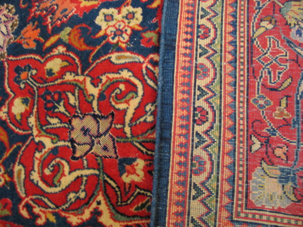 Detailed view of a plush red and blue floral rug contrasting with a narrow, tightly woven geometric border.