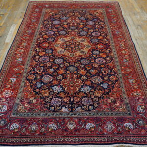 A detailed red and navy blue floral medallion rug rests on worn light hardwood flooring.