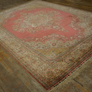 Ornate salmon and beige patterned area rug with visible fringe rests on distressed wood plank flooring.