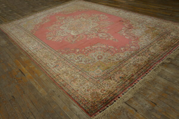 Ornate salmon and beige patterned area rug with visible fringe rests on distressed wood plank flooring.