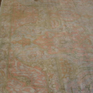 A muted traditional rug in faded pink, cream, and olive green rests on a dark wood floor.