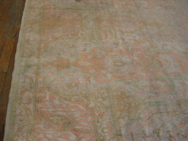 A muted traditional rug in faded pink, cream, and olive green rests on a dark wood floor.