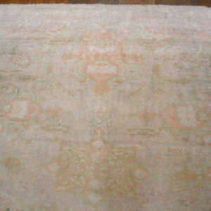 Low-pile distressed rug featuring traditional patterns in faded coral, ivory, and muted green on wood floor.